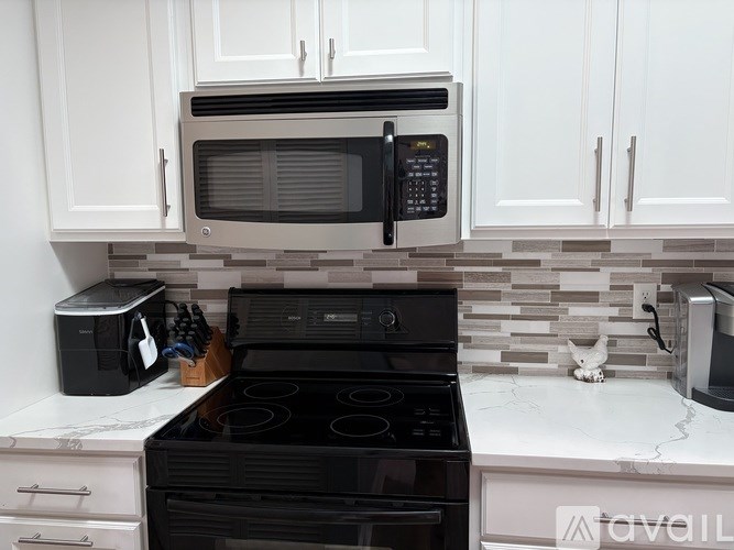 A black microwave is mounted above a black stove in a kitchen with white cabinets.