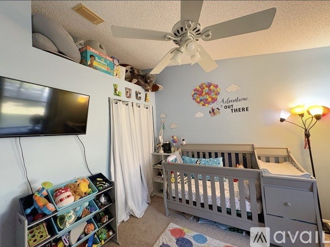 A baby's room with a white crib, a television, a shelf with toys, and a wall decal that says "Adventure Out There".