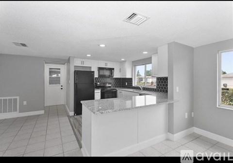 A modern kitchen with a black refrigerator and white cabinets.