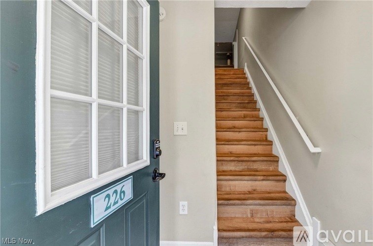 A wooden staircase leads up to a white door with a number plate on it.