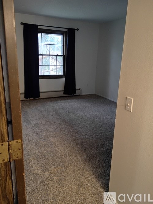 A room with a carpeted floor, a window with black curtains, and a door with a lock.