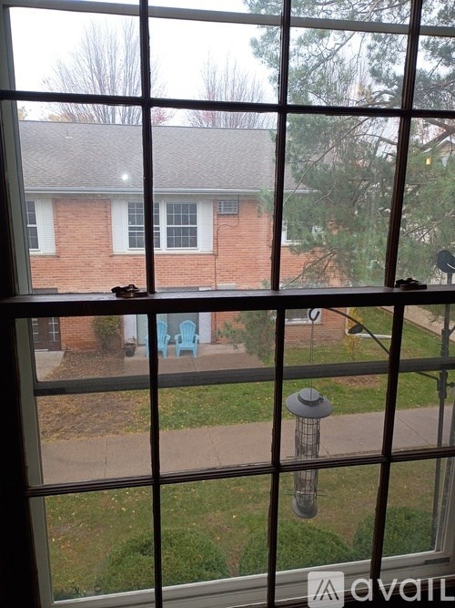 A view from a window looking out to a brick house and a blue chair.