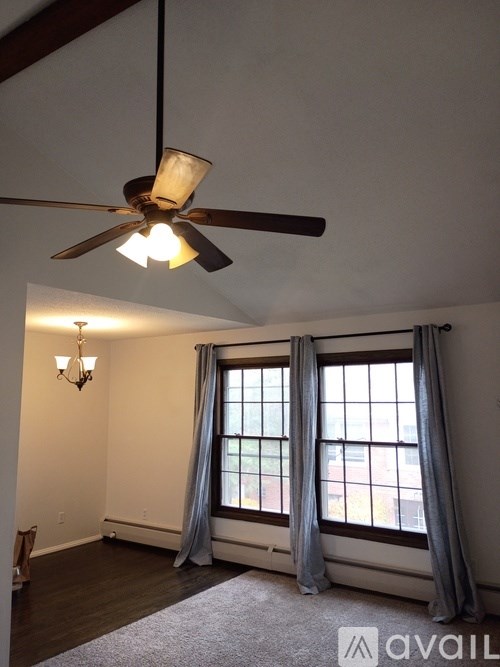A room with a ceiling fan and a window with curtains.
