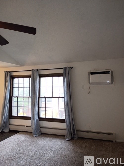 A room with a carpeted floor, a window with curtains, and a ceiling fan.