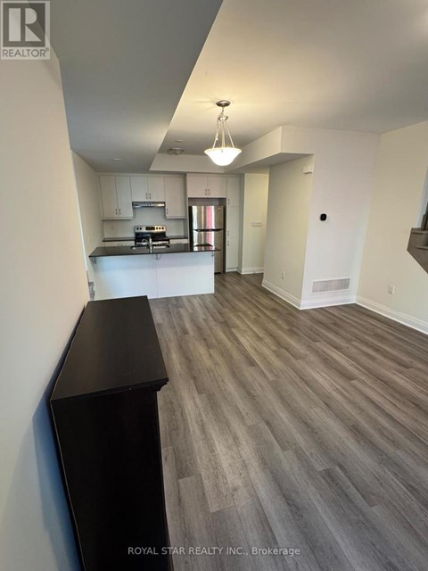 A spacious living room with wood flooring and a kitchen area in the background.