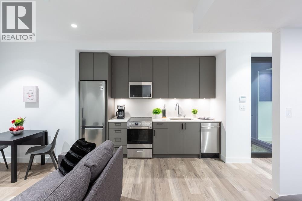 A modern kitchen with a grey couch and wooden flooring.