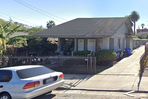 A silver car is parked in front of a house with a fence.