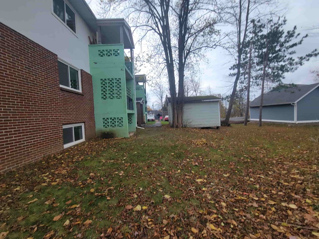 A green electrical box sits on a grassy area in front of a brick building.