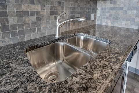 A modern kitchen sink with a granite countertop and a silver faucet.