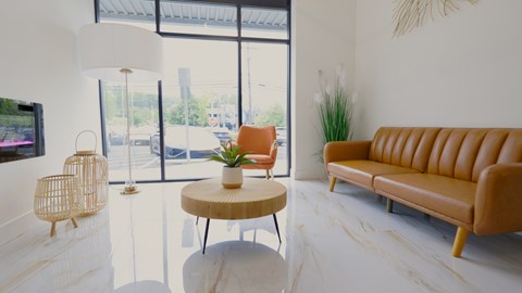 A living room with a tan couch, a white table, and a TV on the wall.