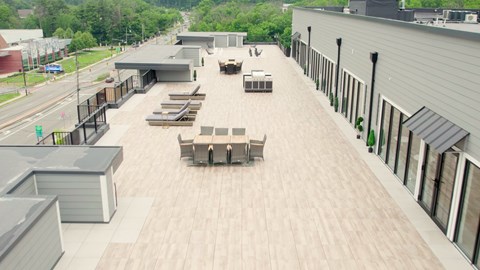 A rooftop patio with wooden furniture and a grey building in the background.