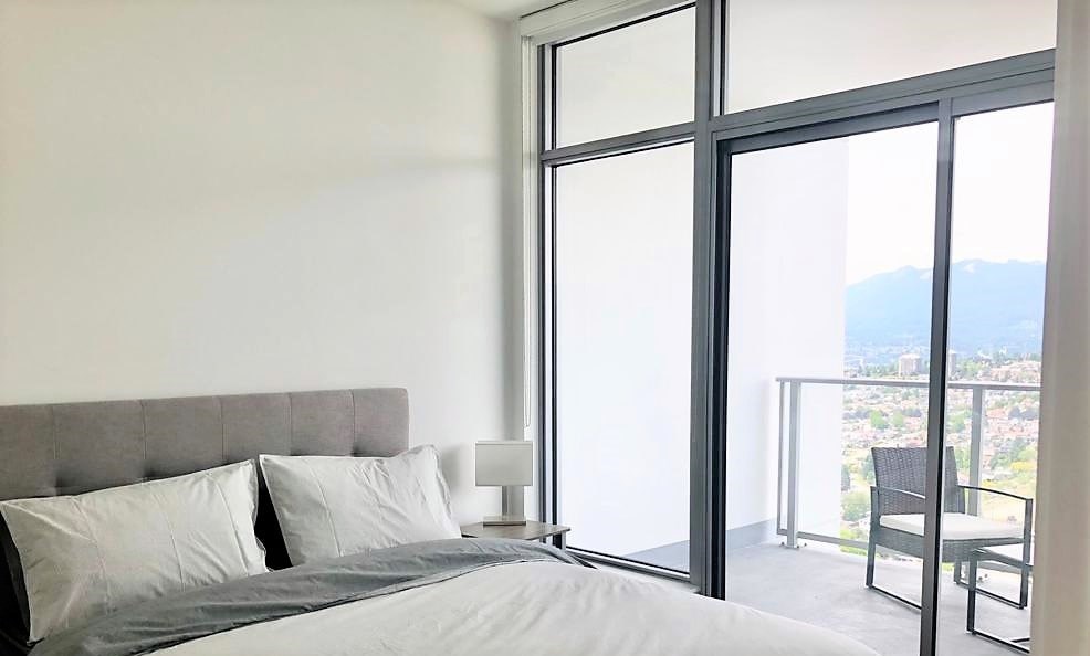 A bedroom with a large bed and a balcony overlooking the city.