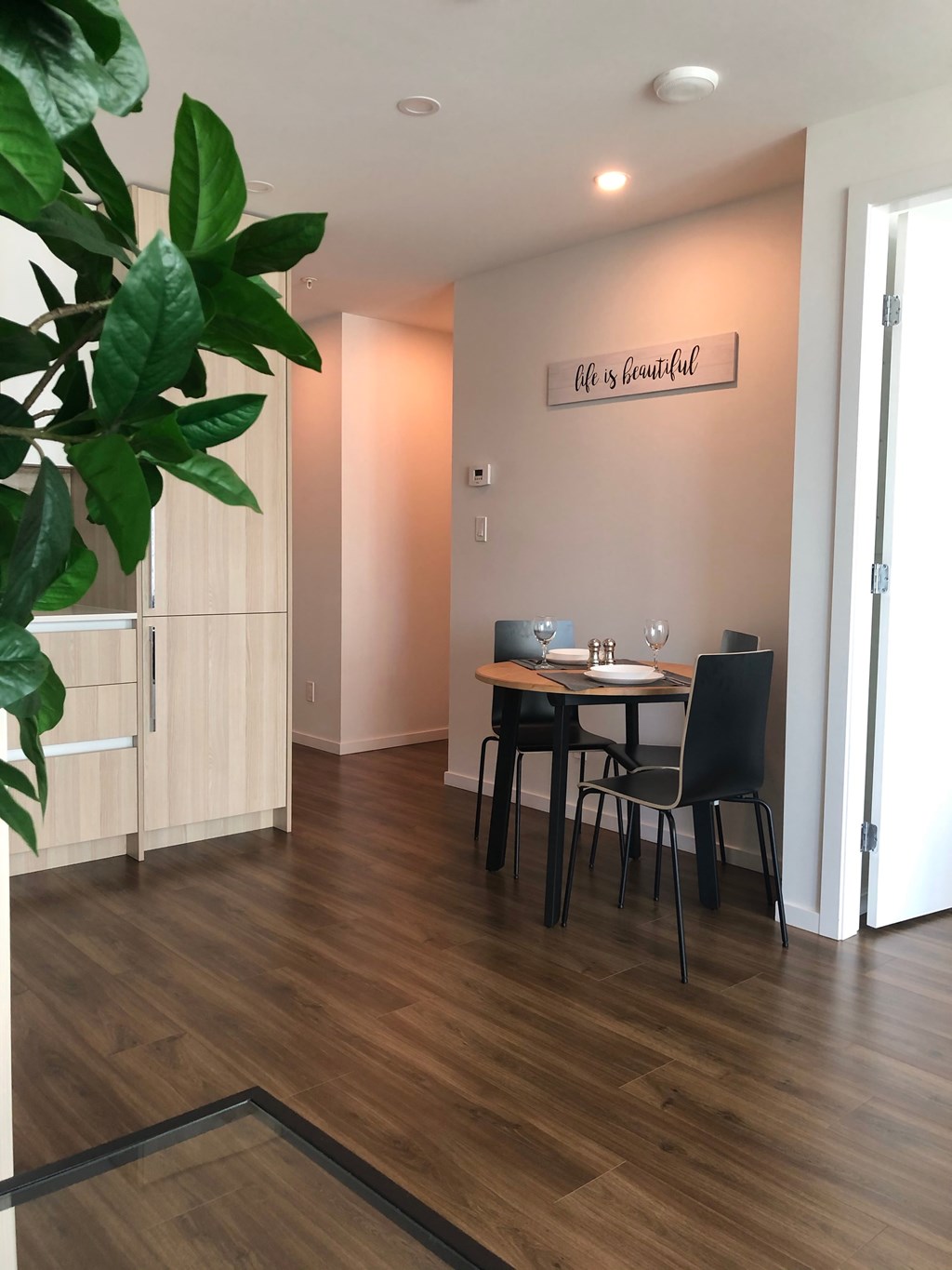 A dining room with a table set for two and a plant in the corner.