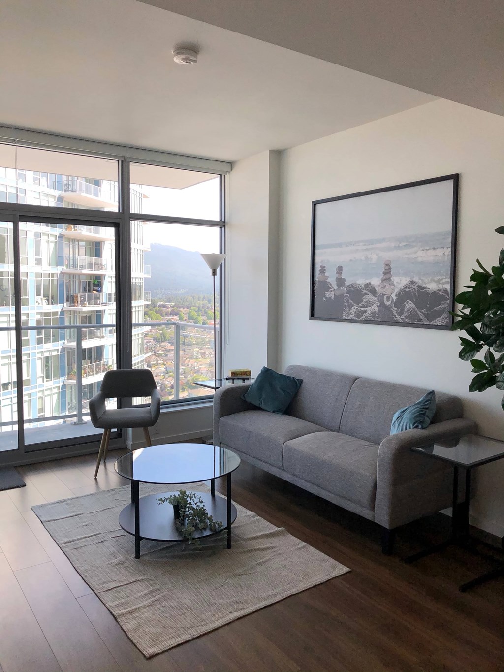 A living room with a grey couch, a coffee table, and a large window overlooking a cityscape.