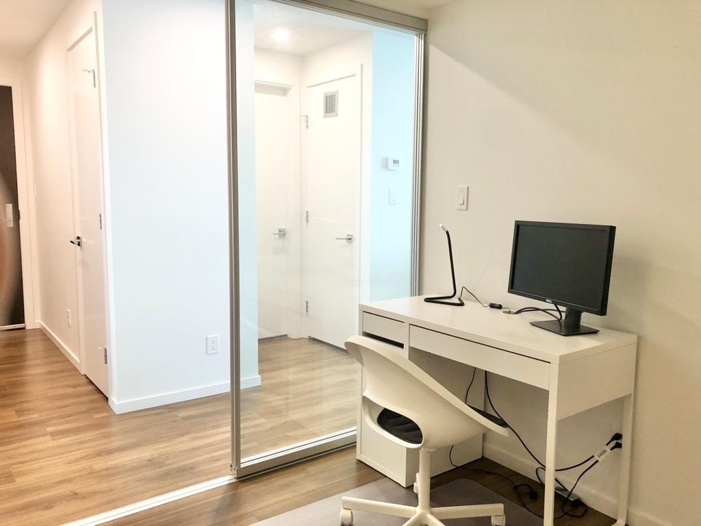 A white desk with a computer monitor and keyboard sits in a room with a sliding glass door.