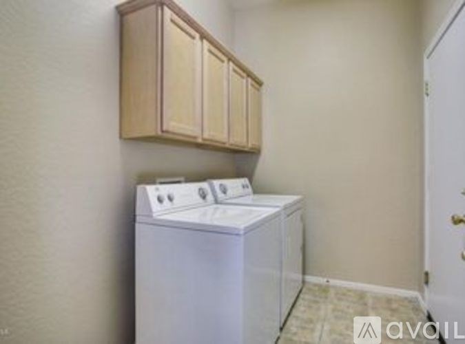 A white dryer is in a small room with a cabinet above it.