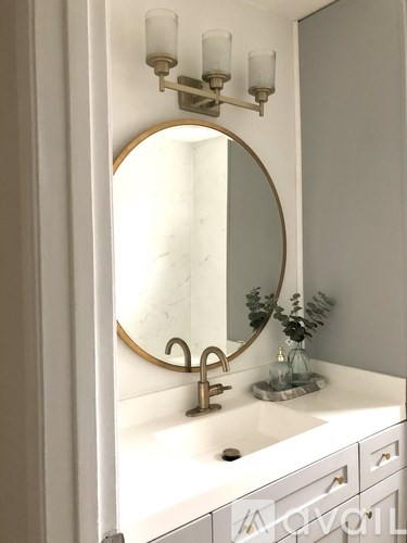 A bathroom vanity with a round mirror and a wall-mounted light fixture.