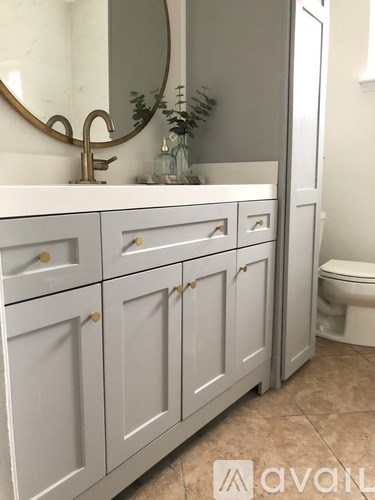 A bathroom with a white cabinet and a round mirror above the sink.