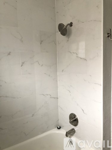 A white marble tiled shower with a shower head and faucet.