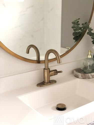 A bathroom sink with a gold faucet and a round mirror above it.