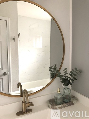 A bathroom sink with a round mirror and a plant.