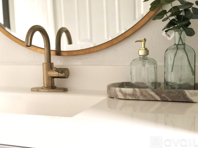 A bathroom sink with a round mirror above it and two bottles on the counter.