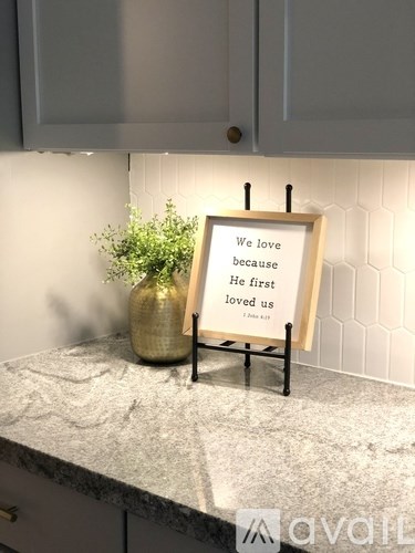 A framed sign that reads "We love because He first loved us" is displayed on a kitchen counter.