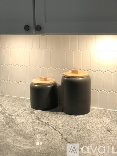Two black containers with wooden lids sit on a marble countertop.