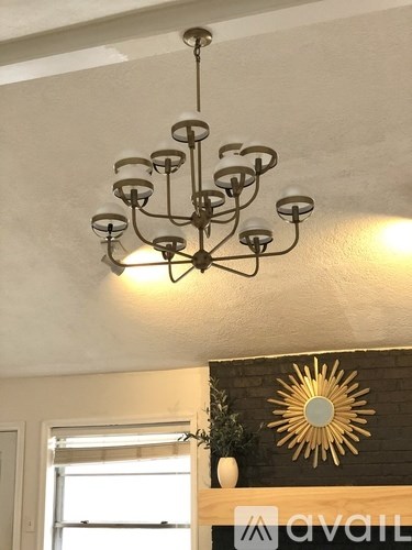 A chandelier hangs from the ceiling in a room with a sunburst mirror on the wall.