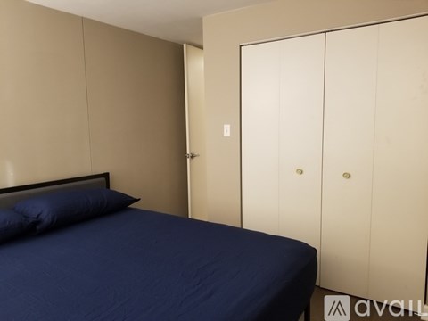 A bed with a dark blue cover sits in a room with a white door and a wall with a brown panel.