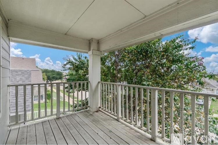 A wooden deck with a white railing and a view of a green tree and a house.