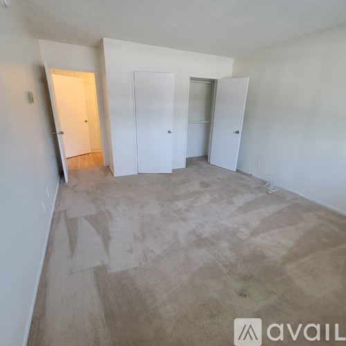 A room with white walls and carpeted floor with four doors.