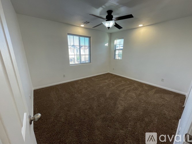 A room with a carpeted floor, a ceiling fan, and two windows.