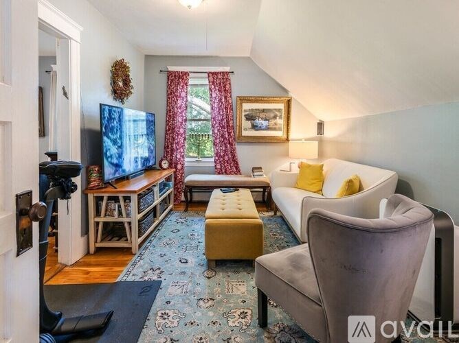 A living room with a grey couch, a yellow ottoman, a television, and a painting on the wall.