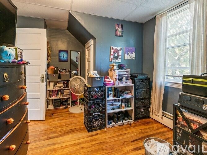 A room with a lot of items including a fan, a bookshelf, and a dresser.