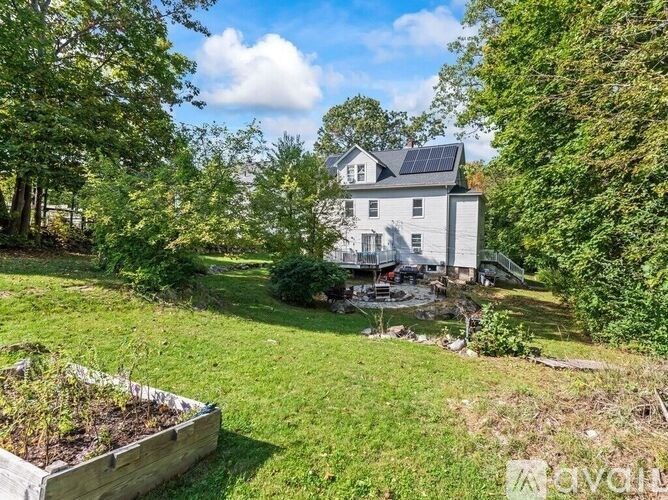 A house with a solar panel on the roof is surrounded by greenery.