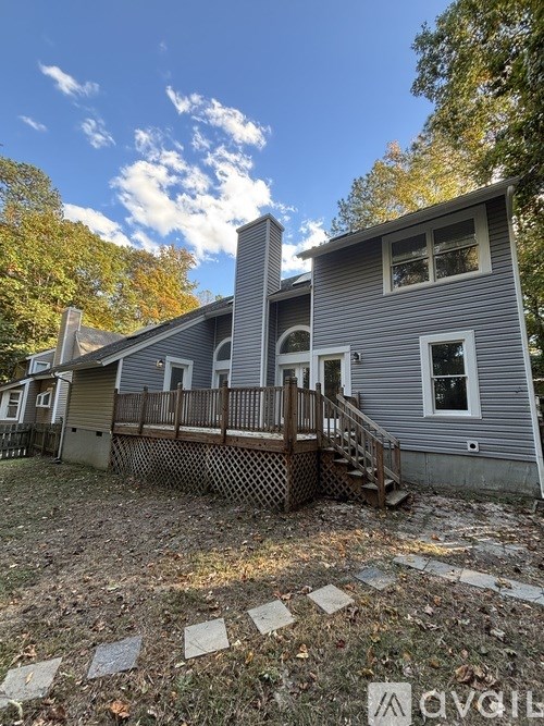 A grey house with a wooden deck and a chimney.