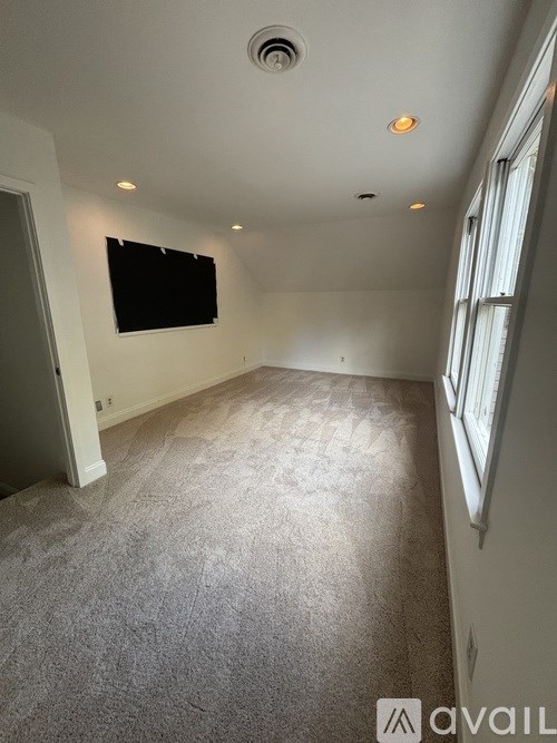 A room with a carpeted floor and a flat screen TV mounted on the wall.
