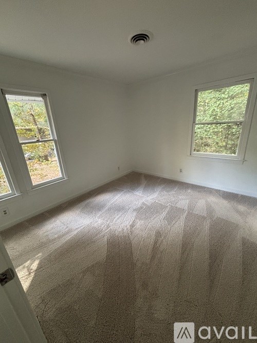 A room with a carpeted floor and two windows.