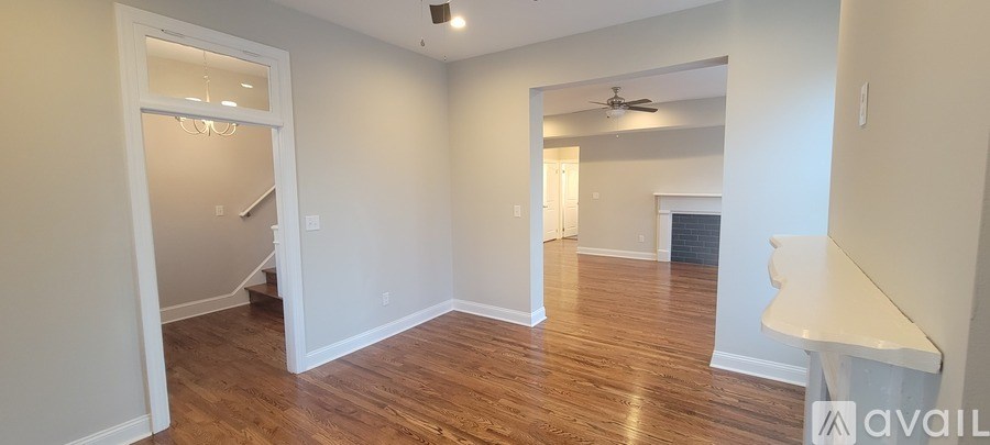 A spacious room with wood flooring and a staircase in the background.