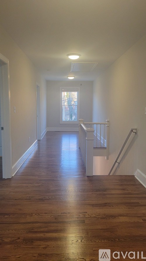 A long hallway with wooden floors and a window at the end.