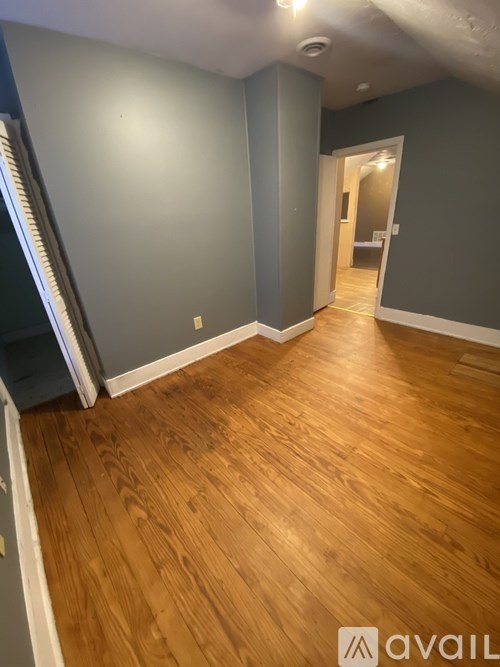 A room with wooden flooring and a doorway leading to another room.