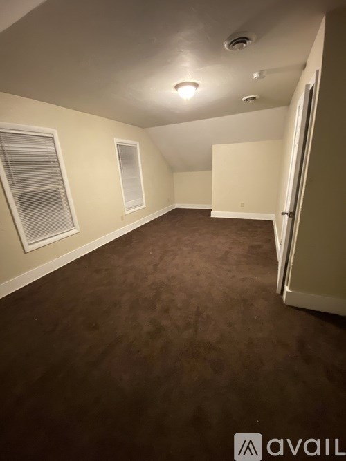 A room with brown carpeting and a window with blinds.