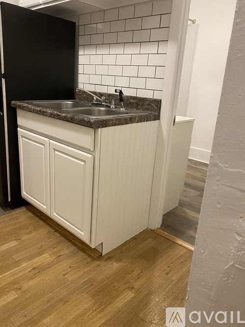 A kitchen with a black refrigerator, white cabinets, and a marble countertop.