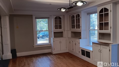 A room with wooden floors and white cabinets with windows.