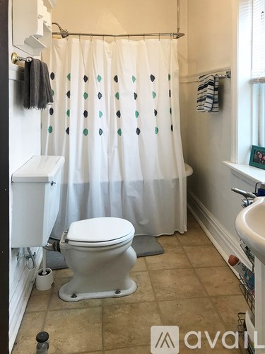 A white toilet sits in a bathroom with a shower curtain that has green dots on it.
