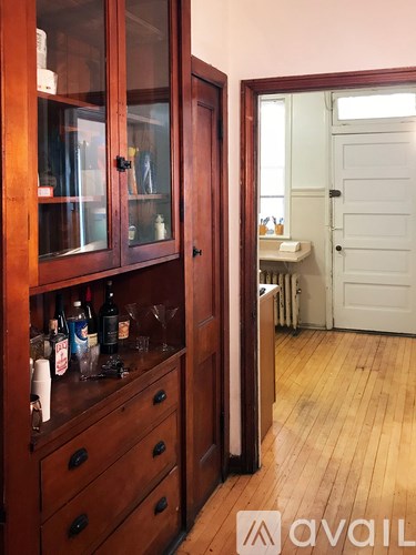 A brown cabinet with glass doors and drawers is full of bottles and glasses.