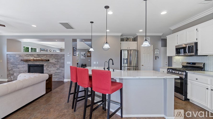 A kitchen with a white island and red chairs.
