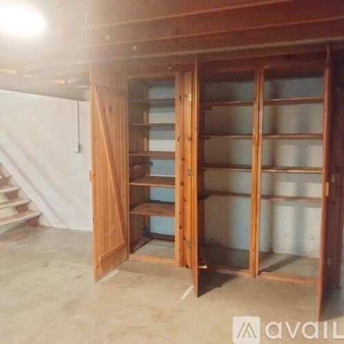 A wooden shelving unit with glass doors is open in a room under construction.