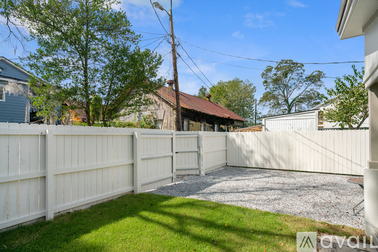 A white fence encloses a yard with a gravel path and green grass.